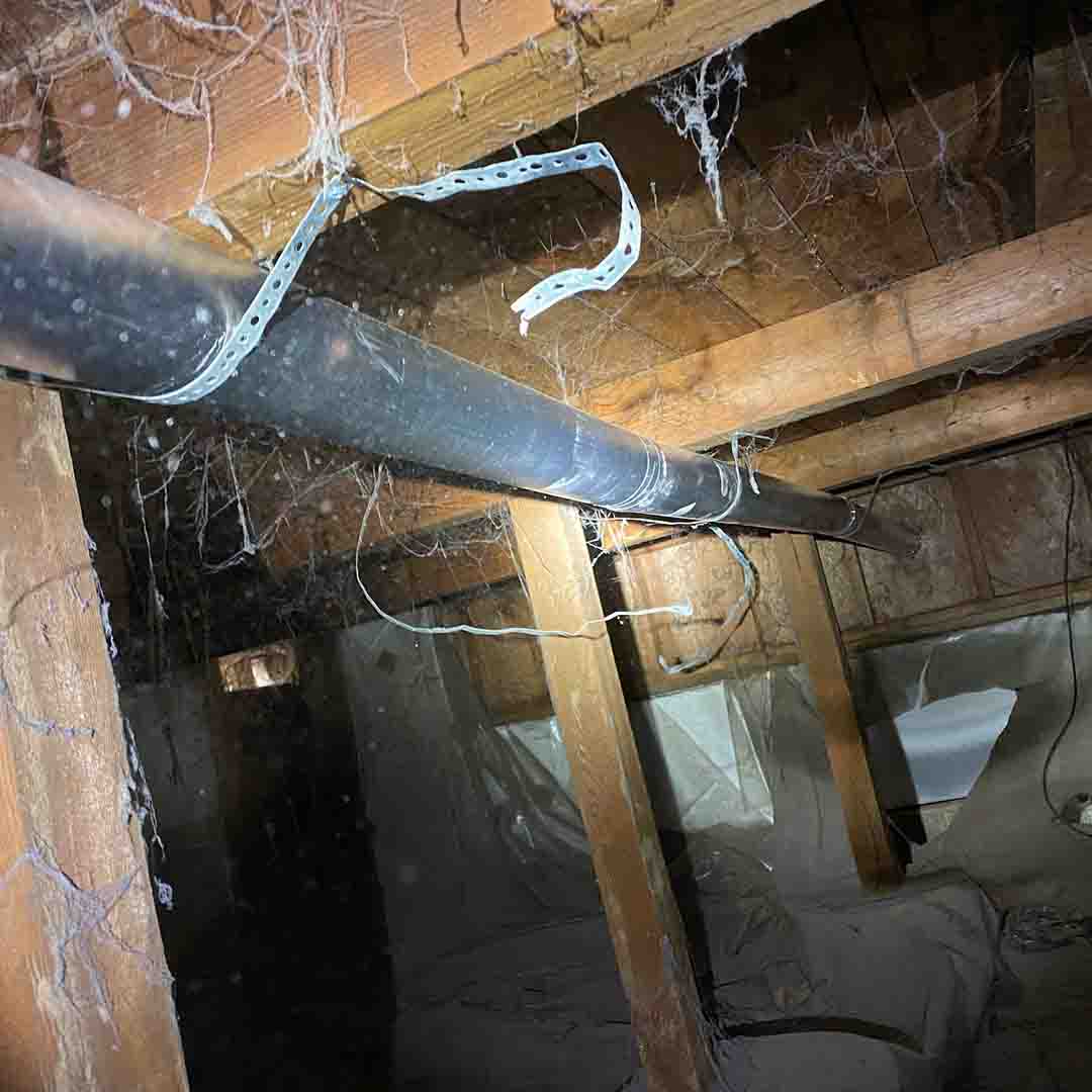 A silver metal dryer vent transition pipe in the crawlspace of a home. There is silver metal duct tape on the pipe where it has been repaired.
