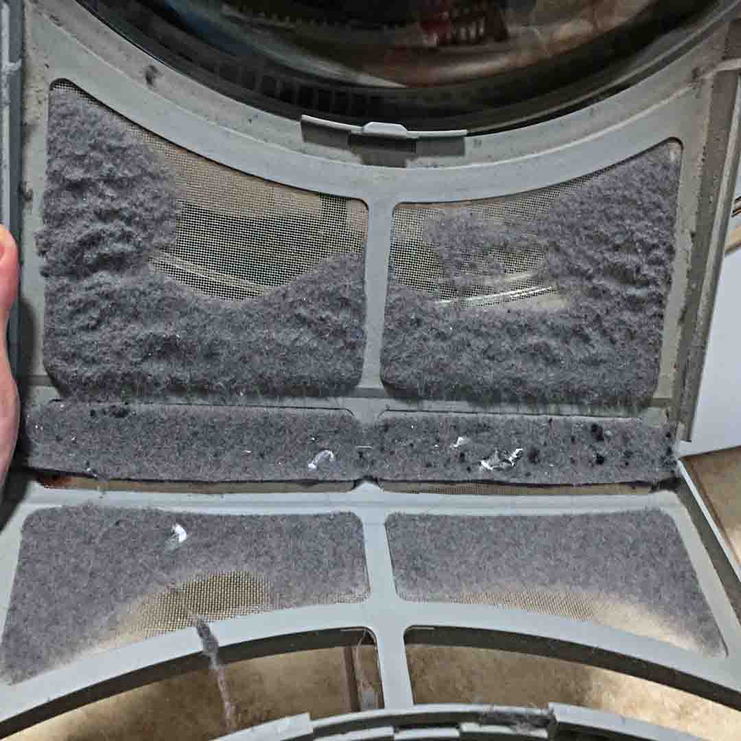 Two hands hold a dryer lint trap which has not been cleaned.