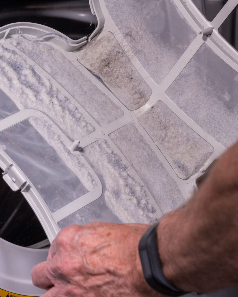 Two hands hold a dryer lint trap which has not been cleaned.