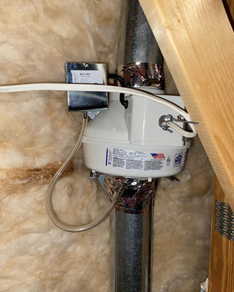 An outside view of a booster fan connected to a dryer vent hose. Silver metal duct tape can be seen where a repair has been made.