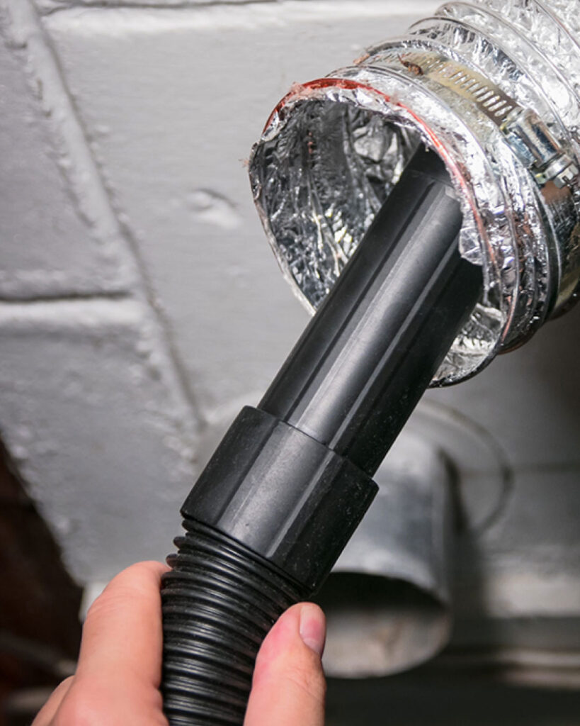 A technician vacuums out a dryer vent hose.