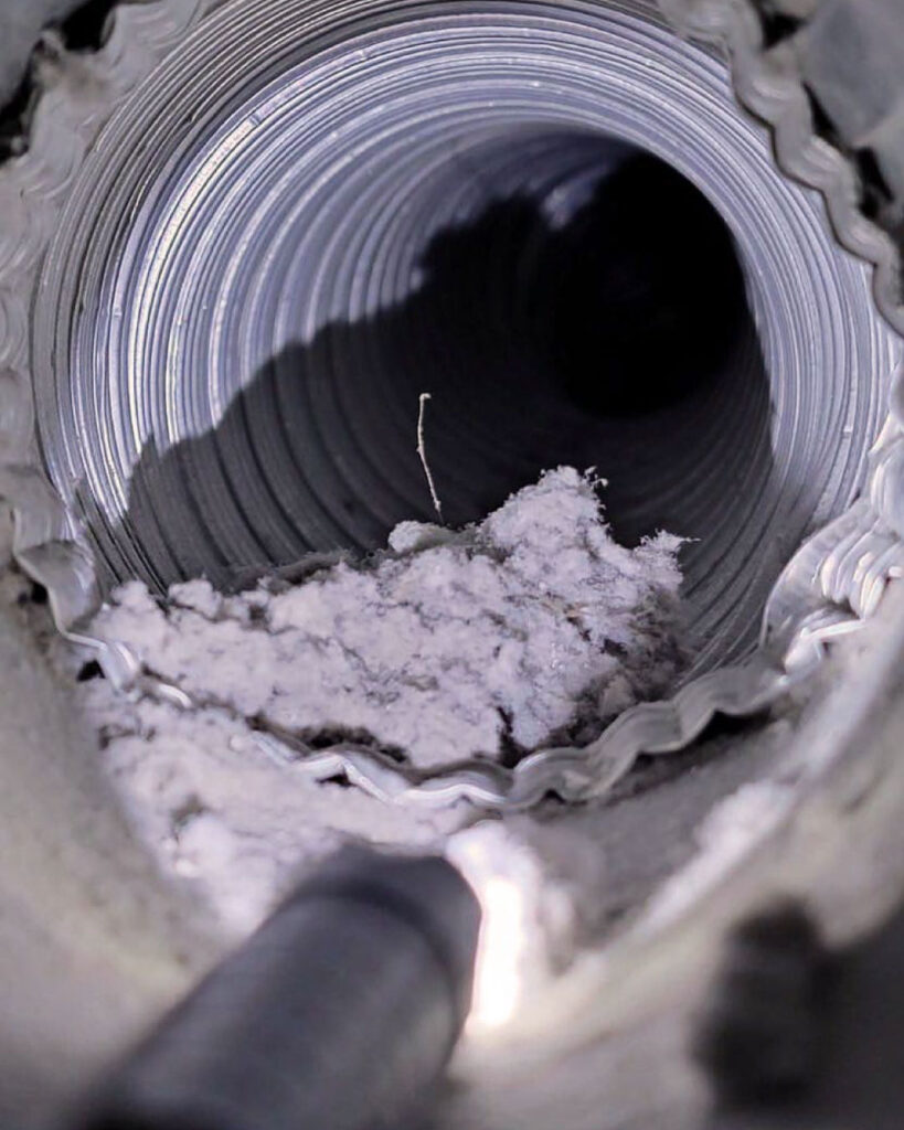 An interior shot of a silver metal dryer vent hose with lint build up inside.