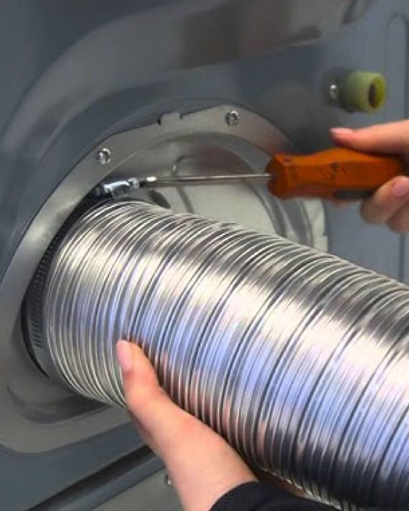 A technician installs a brand new silver metal dryer vent hose behind a dryer in a home. Environment is clean and white.