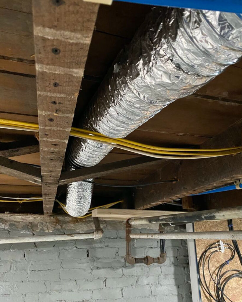 A silver metal dryer vent transition pipe in the basement of a home.