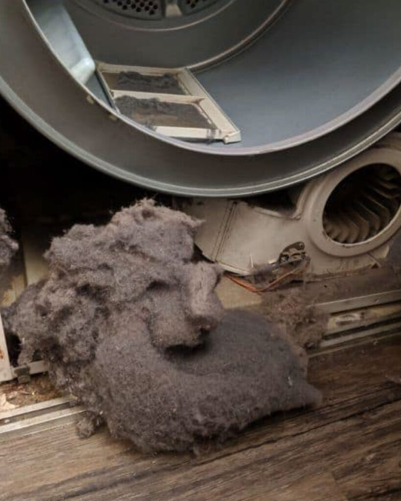 Lint lays on the ground after a technician has cleaned out the lint trap and interior of a dryer.