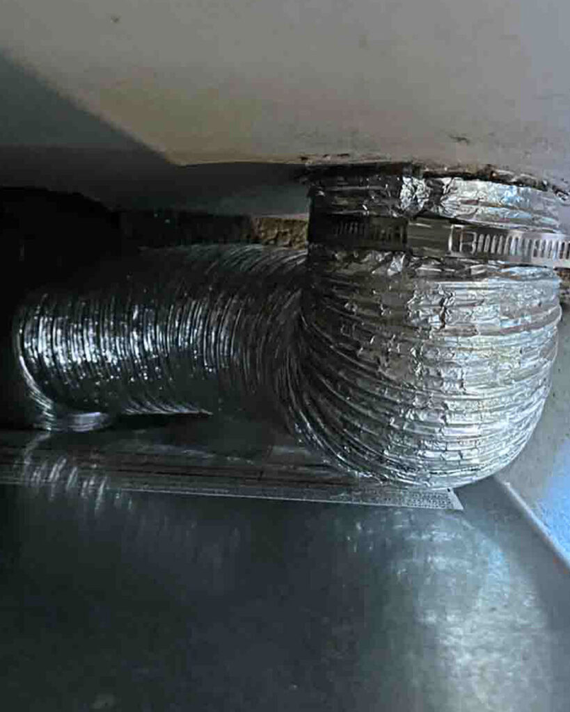 An up-close shot of a dryer vent transition hose behind a dryer .