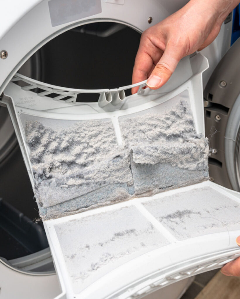 Two hands hold a dryer lint trap which has not been cleaned.