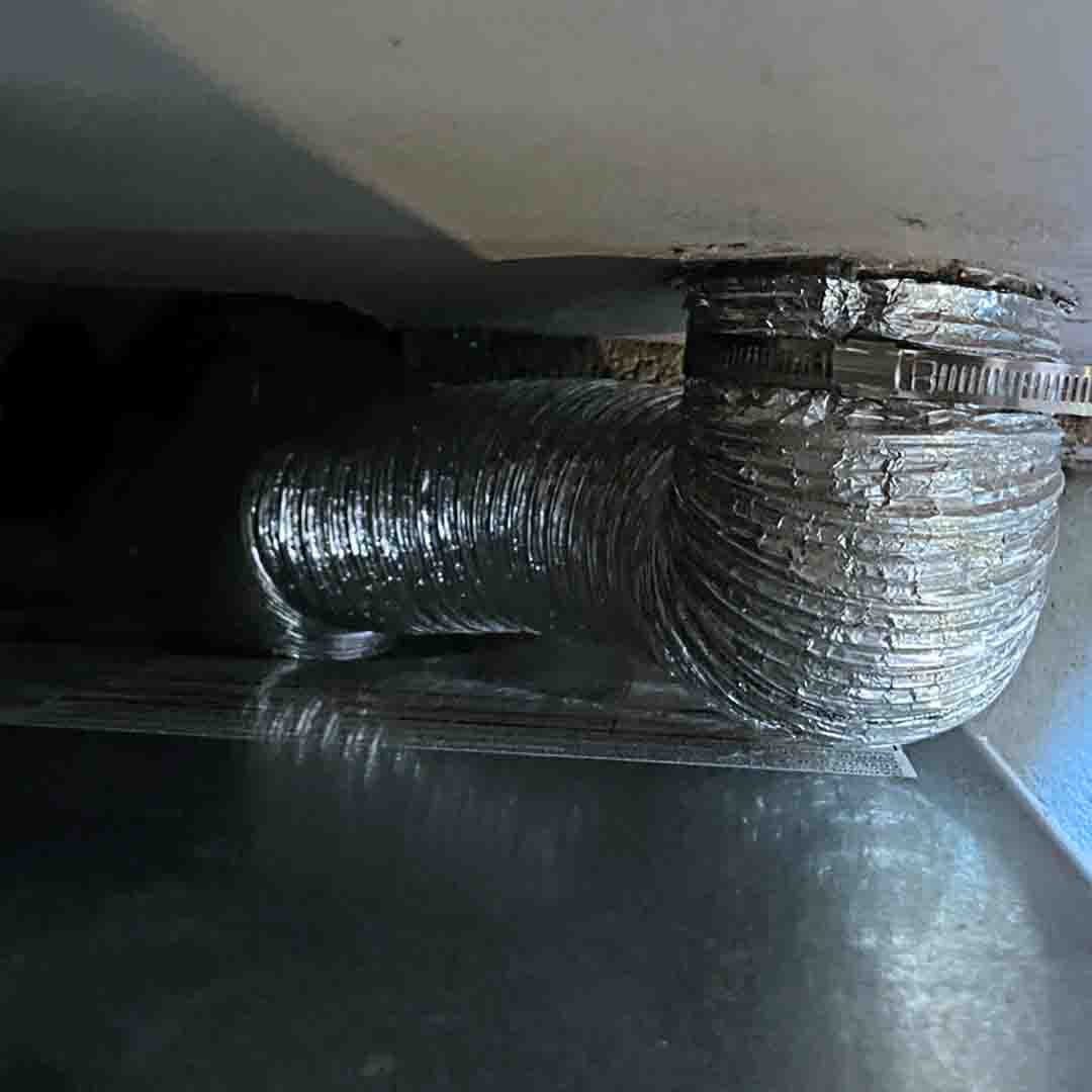 An up-close shot of a dryer vent transition hose behind a dryer .