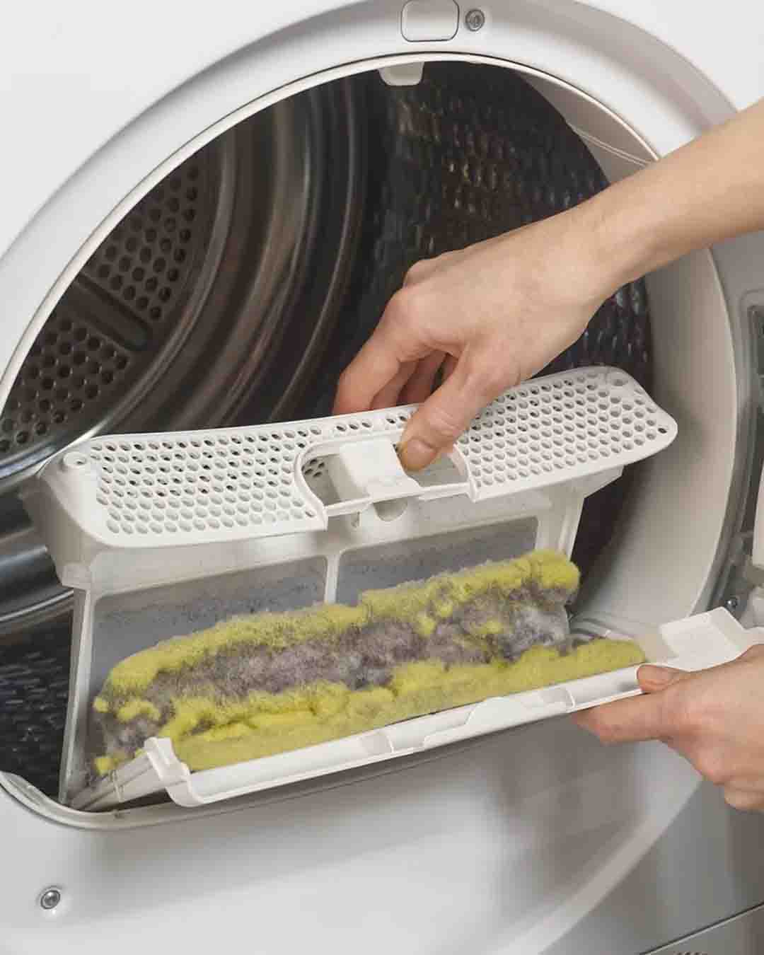 Two hands hold a dryer lint trap which has not been cleaned.